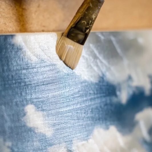 A brush applying hand-finished acrylic gel to a canvas.